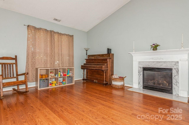 sitting room featuring visible vents, wood finished floors, baseboards, high vaulted ceiling, and a premium fireplace