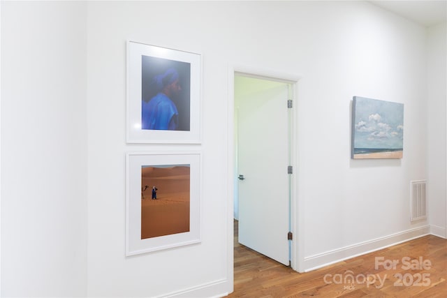 hall featuring light wood-style floors, baseboards, and visible vents
