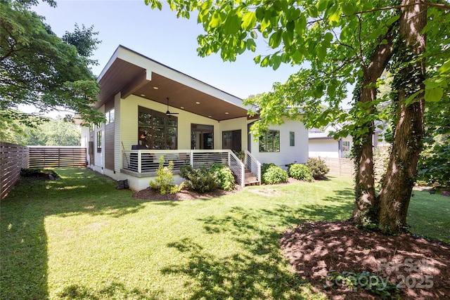 rear view of property featuring fence, a ceiling fan, and a yard