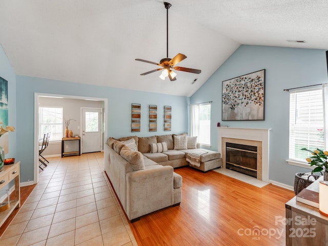 living area with a ceiling fan, a fireplace, healthy amount of natural light, baseboards, and high vaulted ceiling