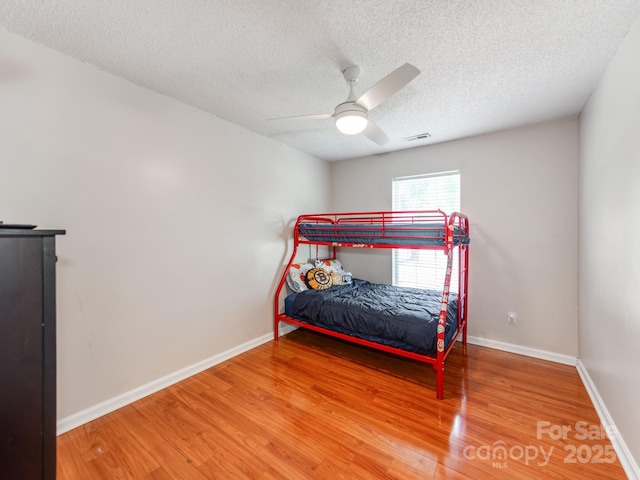 bedroom featuring wood finished floors, a textured ceiling, baseboards, and ceiling fan