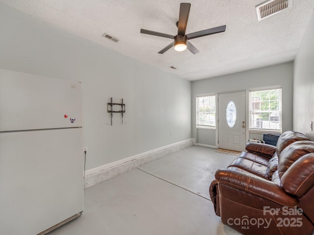 living area with a textured ceiling, a ceiling fan, concrete floors, and baseboards
