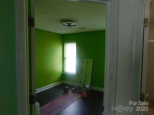 empty room featuring a textured ceiling, baseboards, visible vents, and wood finished floors