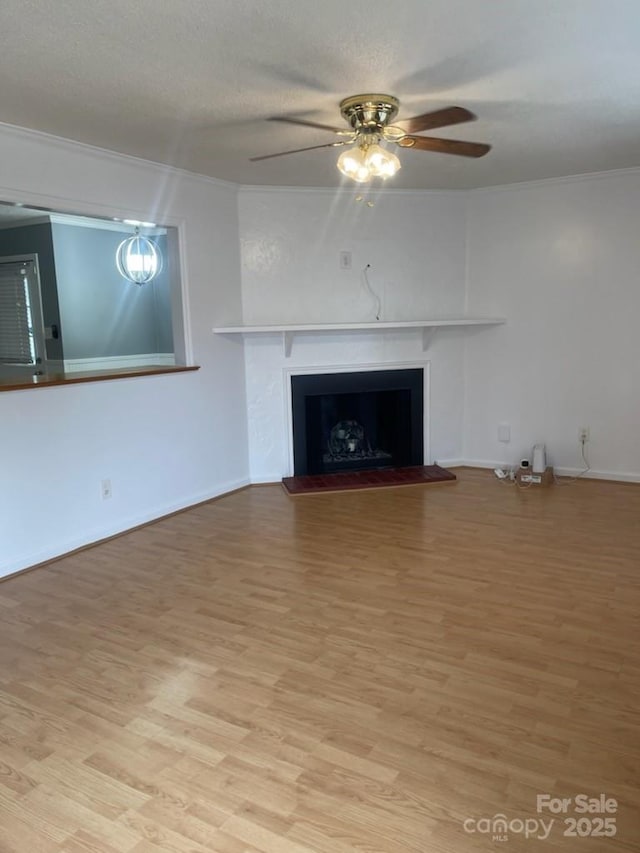 unfurnished living room featuring ornamental molding, light wood finished floors, ceiling fan, and a fireplace with raised hearth