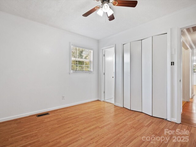 unfurnished bedroom with light wood-style flooring, ceiling fan, baseboards, visible vents, and crown molding