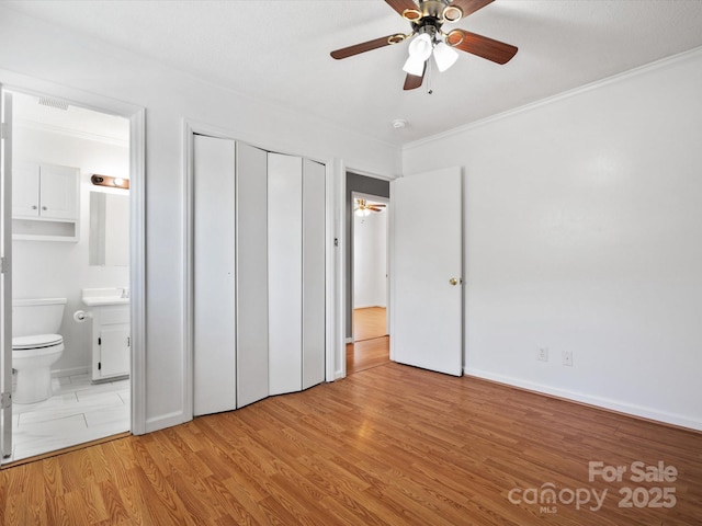 unfurnished bedroom with wood finished floors, connected bathroom, a closet, a ceiling fan, and crown molding