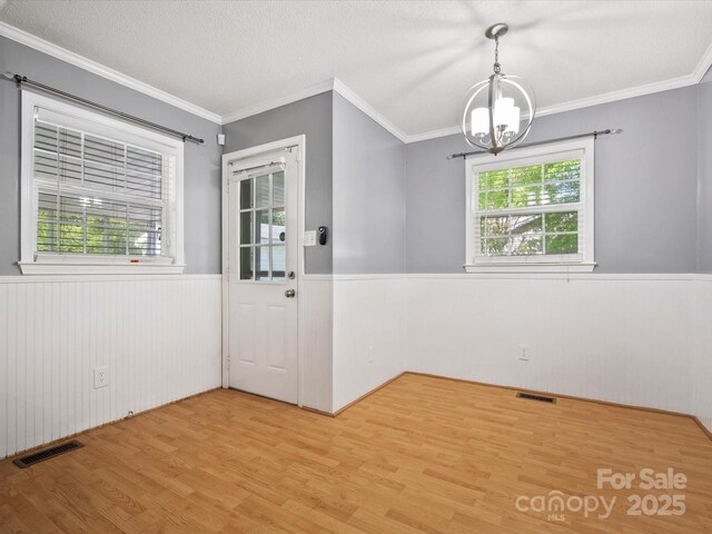 unfurnished dining area featuring a chandelier, visible vents, a wainscoted wall, and light wood-style flooring