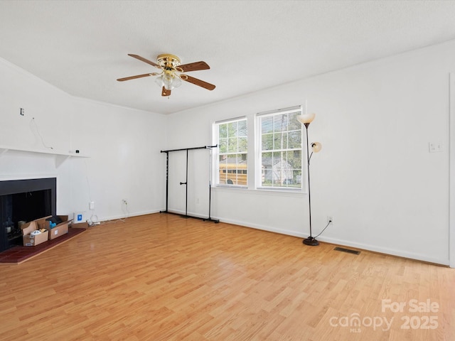 unfurnished living room featuring a fireplace with raised hearth, ceiling fan, light wood-style flooring, and baseboards