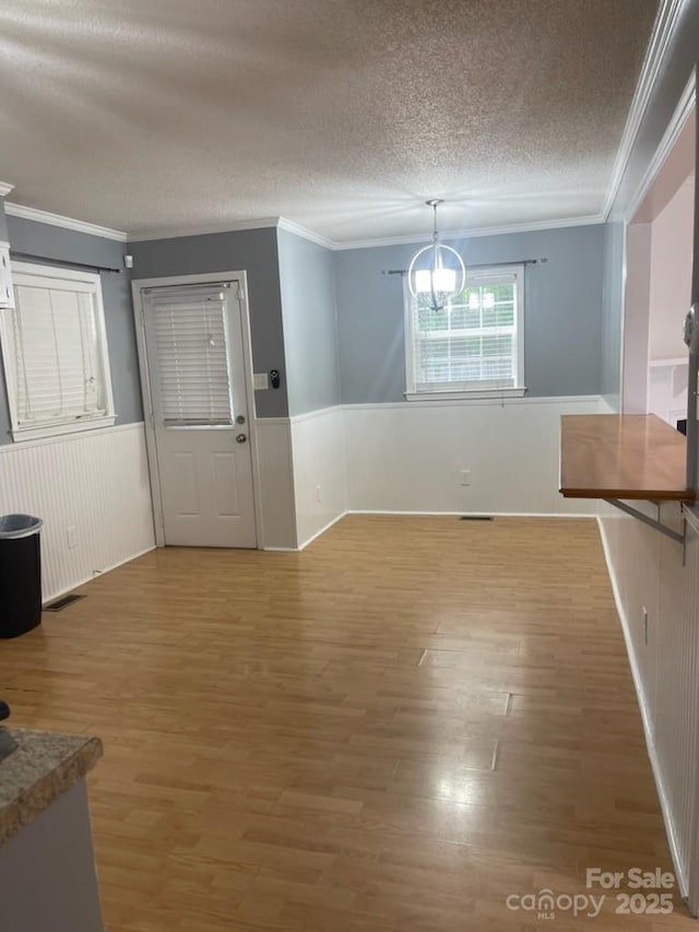 unfurnished dining area with ornamental molding, a wainscoted wall, a textured ceiling, and light wood finished floors