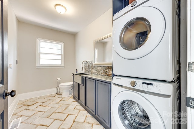 washroom with cabinet space, a sink, brick floor, baseboards, and stacked washer / dryer