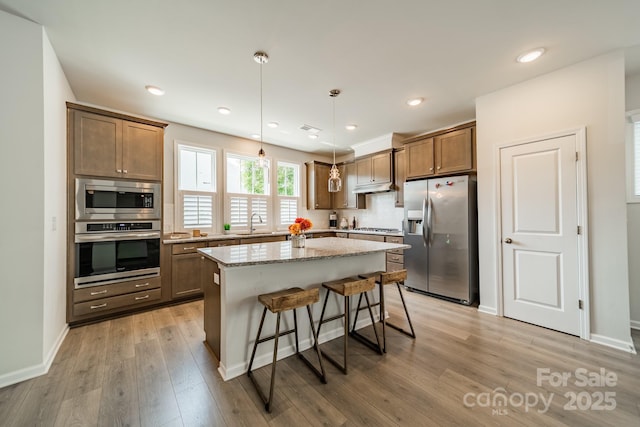 804 Lyndon Station Dr, Pineville, NC 28134 - kitchen featuring light stone counters, appliances with stainless steel finishes, a kitchen breakfast bar, light wood-style flooring, and a center island