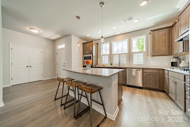 804 Lyndon Station Dr, Pineville, NC 28134 - kitchen with visible vents, appliances with stainless steel finishes, light stone countertops, a breakfast bar, and light wood-style flooring