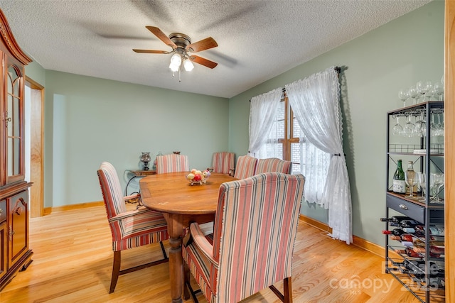dining room featuring a textured ceiling, light wood-type flooring, a ceiling fan, and baseboards
