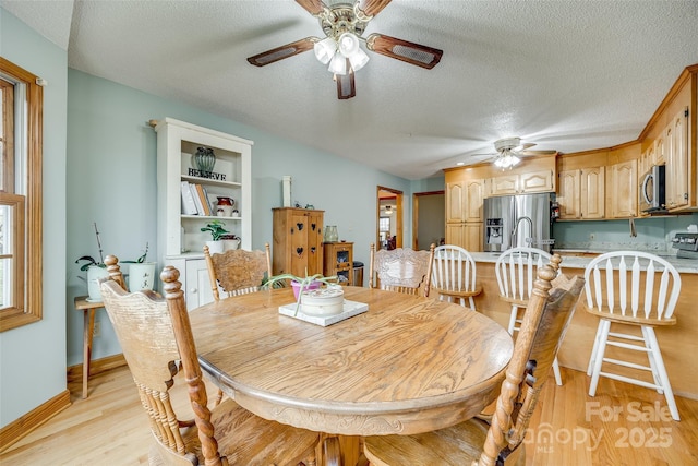 dining room featuring a textured ceiling, ceiling fan, light wood finished floors, and baseboards