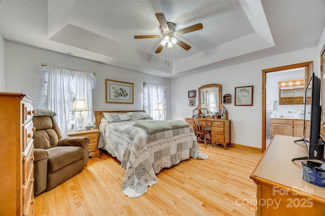 bedroom featuring light wood-style floors, a tray ceiling, a ceiling fan, baseboards, and a textured ceiling