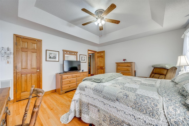 bedroom featuring light wood finished floors, baseboards, visible vents, a raised ceiling, and a ceiling fan