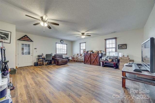 living area with a healthy amount of sunlight, wood finished floors, a ceiling fan, and a textured ceiling