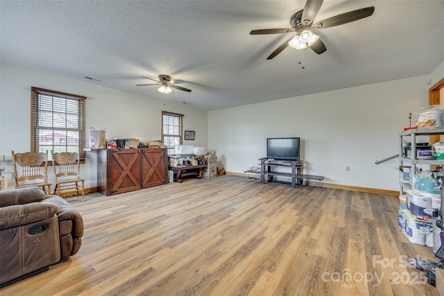 living area with a textured ceiling, ceiling fan, baseboards, and light wood-style floors