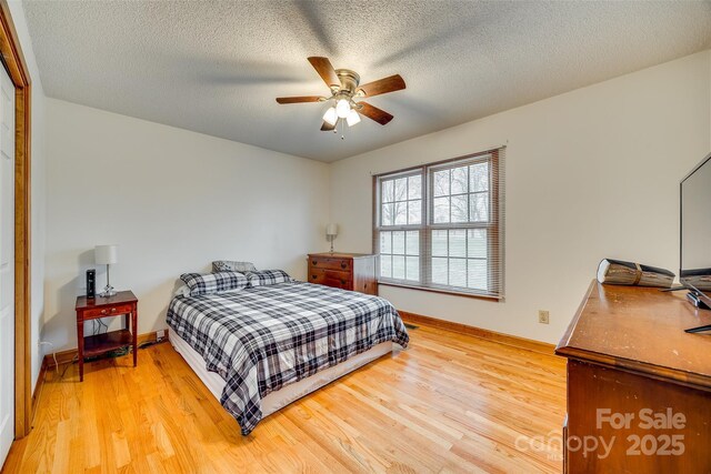 bedroom featuring baseboards, ceiling fan, a textured ceiling, and light wood finished floors