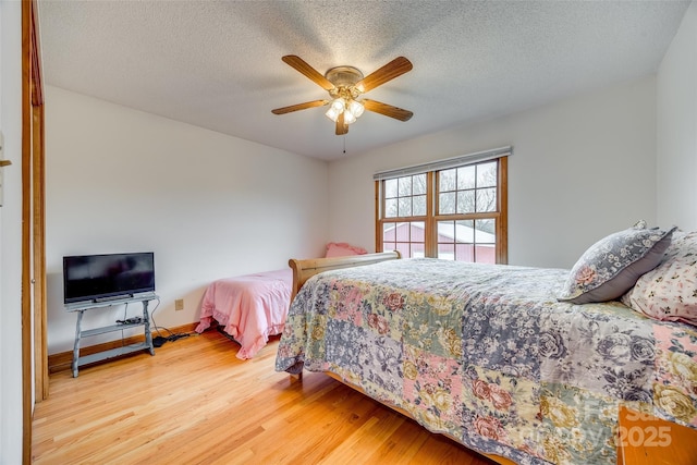 bedroom featuring baseboards, wood finished floors, a ceiling fan, and a textured ceiling