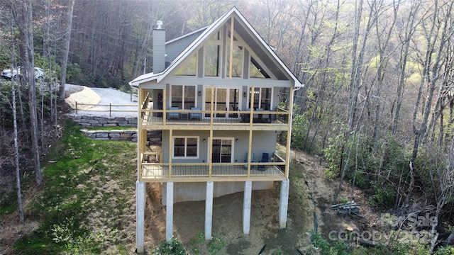 rear view of property with a balcony, a wooden deck, a chimney, and a forest view