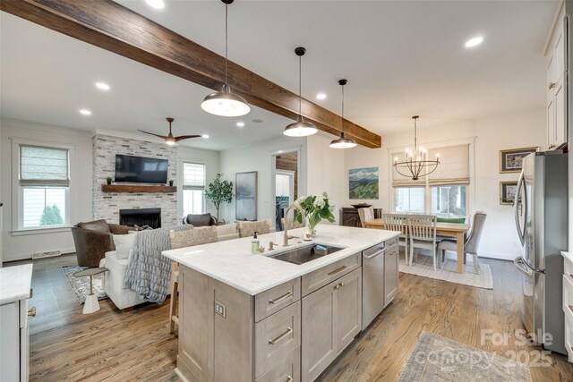 kitchen with a fireplace, wood finished floors, a sink, beamed ceiling, and stainless steel appliances