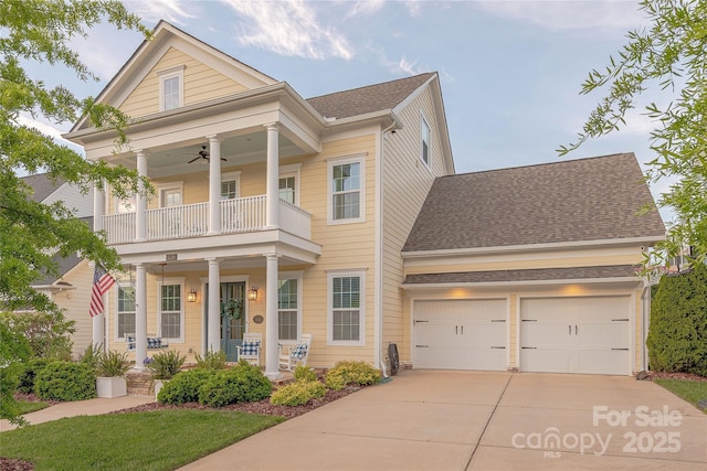 greek revival inspired property with a porch, a shingled roof, a balcony, a ceiling fan, and concrete driveway