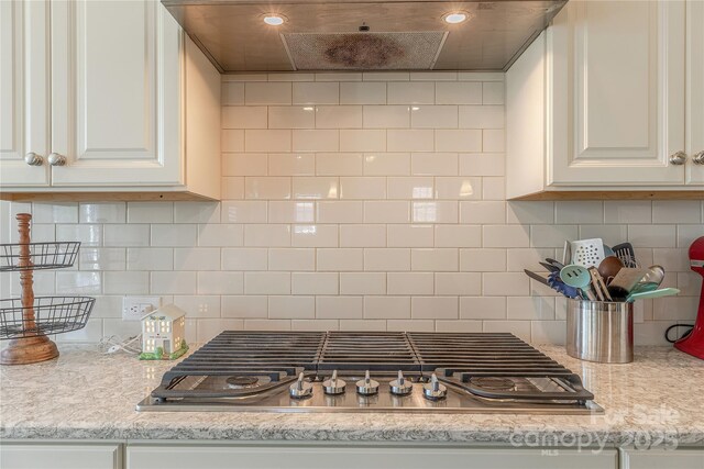 kitchen with backsplash, light countertops, stainless steel gas cooktop, and wall chimney exhaust hood