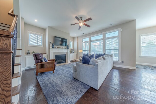 living room with ceiling fan, a fireplace with flush hearth, dark wood-type flooring, and plenty of natural light