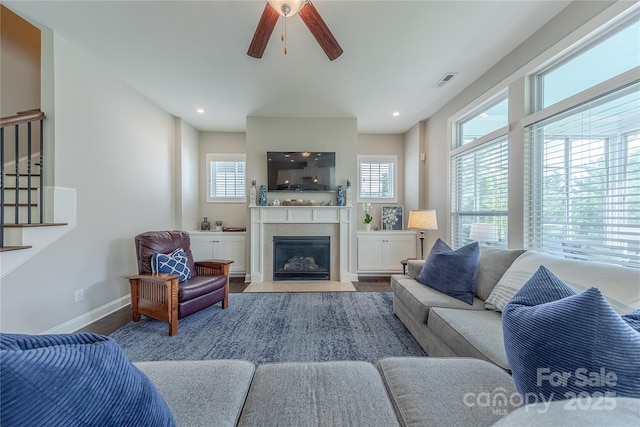 living room featuring a fireplace with flush hearth, ceiling fan, visible vents, baseboards, and wood finished floors