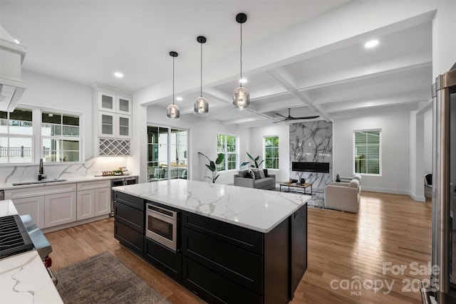 kitchen with stainless steel microwave, white cabinetry, a sink, open floor plan, and light wood finished floors