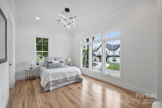 bedroom featuring light wood-style floors, crown molding, a notable chandelier, and multiple windows