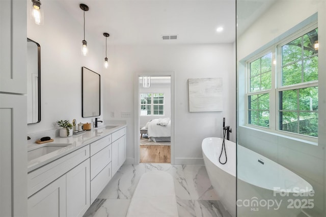ensuite bathroom featuring a sink, double vanity, visible vents, baseboards, and a freestanding tub
