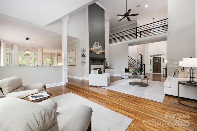 living area with wood finished floors, ceiling fan, a fireplace, baseboards, and a high ceiling