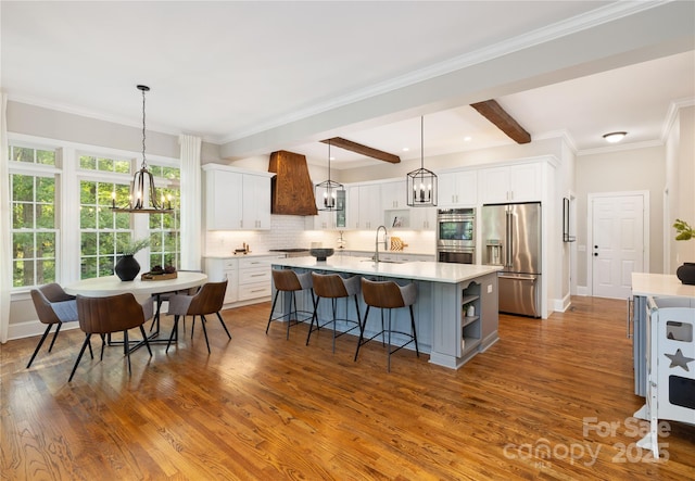 kitchen with white cabinets, a chandelier, stainless steel appliances, a kitchen island with sink, and backsplash