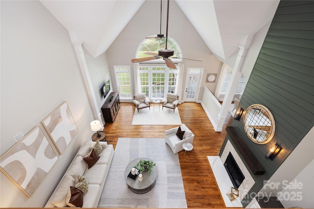 living room with a brick fireplace, high vaulted ceiling, a ceiling fan, baseboards, and wood finished floors