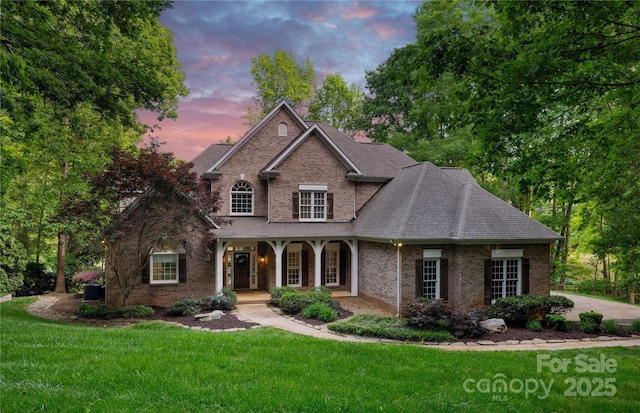 view of front of home featuring a porch, a front lawn, a shingled roof, and brick siding