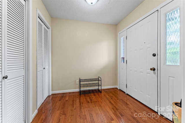 foyer entrance featuring a textured ceiling, wood finished floors, and baseboards