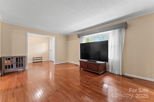 unfurnished living room featuring crown molding, baseboards, hardwood / wood-style floors, and visible vents