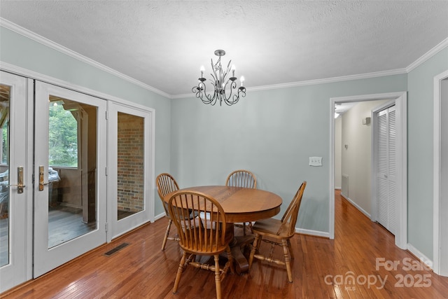 dining area with baseboards, an inviting chandelier, visible vents, crown molding, and wood finished floors