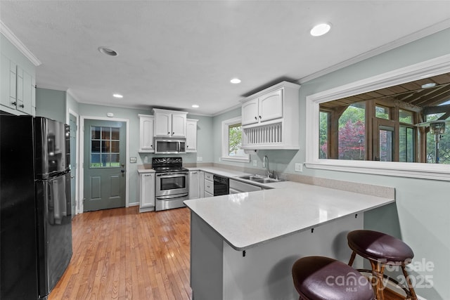 kitchen featuring a breakfast bar, a sink, a peninsula, crown molding, and black appliances