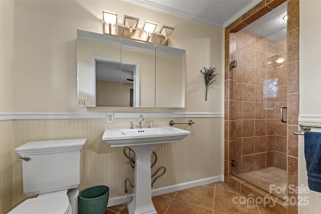 full bath featuring a stall shower, toilet, tile patterned floors, crown molding, and a wainscoted wall