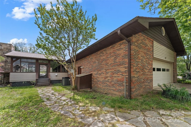 view of home's exterior with brick siding, concrete driveway, a garage, central AC unit, and a sunroom