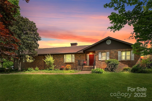 ranch-style home featuring a chimney, a front yard, and brick siding