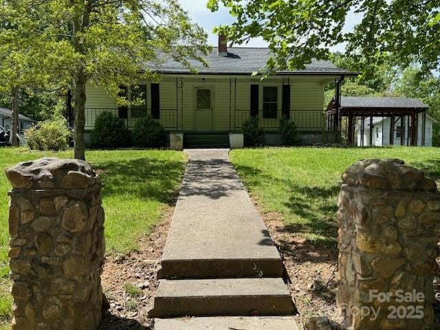view of front of home with a front yard, covered porch, and a chimney