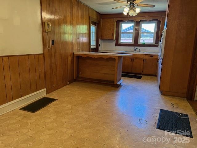 kitchen with wood walls, visible vents, ceiling fan, and brown cabinets