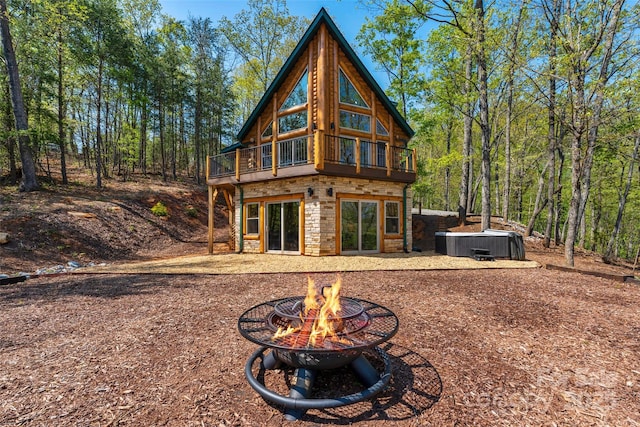 rear view of property with a deck, an outdoor fire pit, central AC, and stone siding
