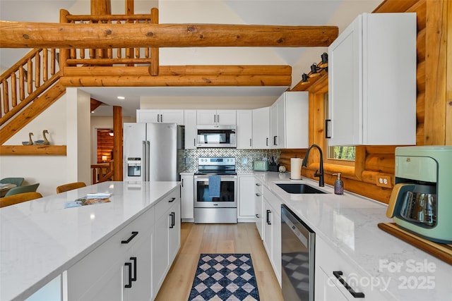 kitchen with light stone counters, a sink, white cabinets, and stainless steel appliances