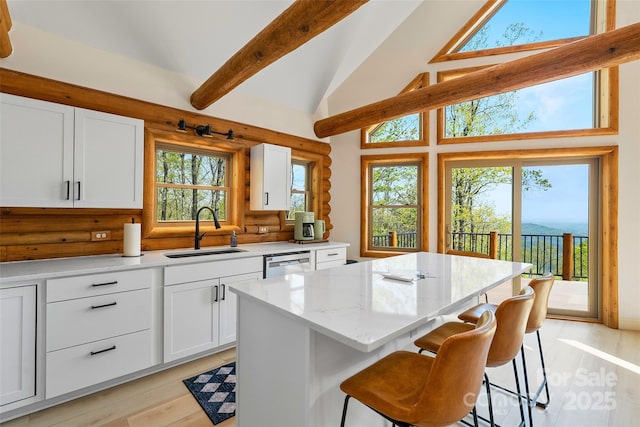kitchen featuring a sink, light wood-style flooring, a center island, white cabinetry, and a kitchen bar