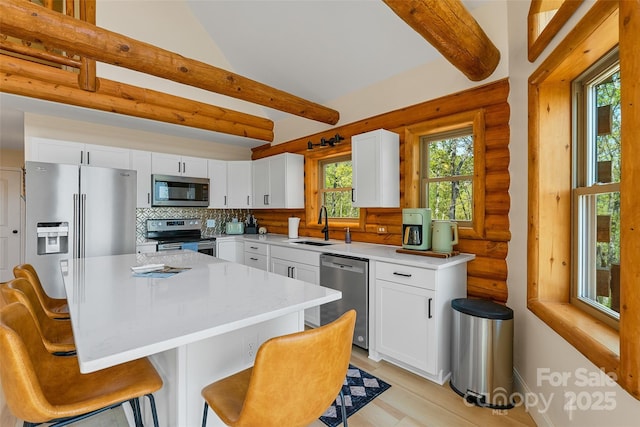 kitchen with a sink, stainless steel appliances, a kitchen bar, beamed ceiling, and log walls